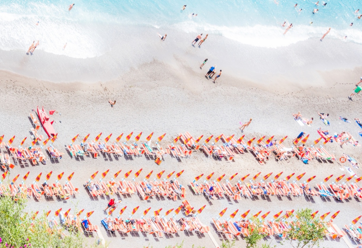 Luftaufnahme einer mediterranen Strandformation mit geometrischen Reihen orangefarbener Sonnenschirme